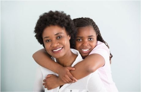 A woman and a girl smile warmly at the camera.