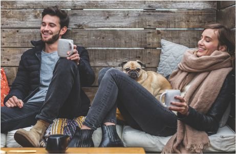 A smiling man and woman sit on a bench with a dog between them.
