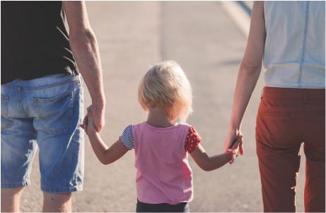 Una niña con camisa rosa se toma de la mano de dos adultos.