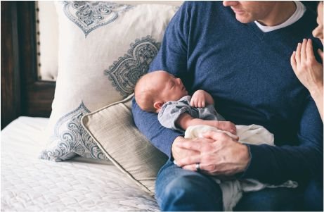 Un hombre con un suéter azul acuna a un recién nacido dormido.