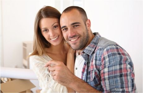 Una pareja sonriente se encuentra en una habitación luminosa, sosteniendo las llaves.