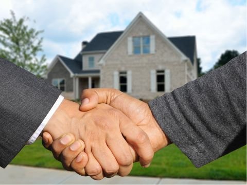 Two people shaking hands in front of a modern brick house.